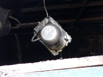 Light fixture hanging by a wiring conduit, viewed through the middle window on the second floor, on the back side.